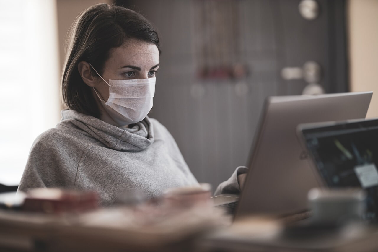 Imagen de una chica que lleva una máscara mientras está sentada frente al ordenador